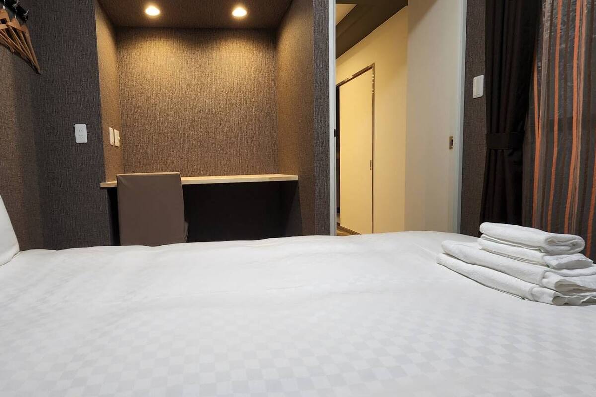 A hotel room with a bed, a small desk, a mirror, and a bathroom visible through an open door.