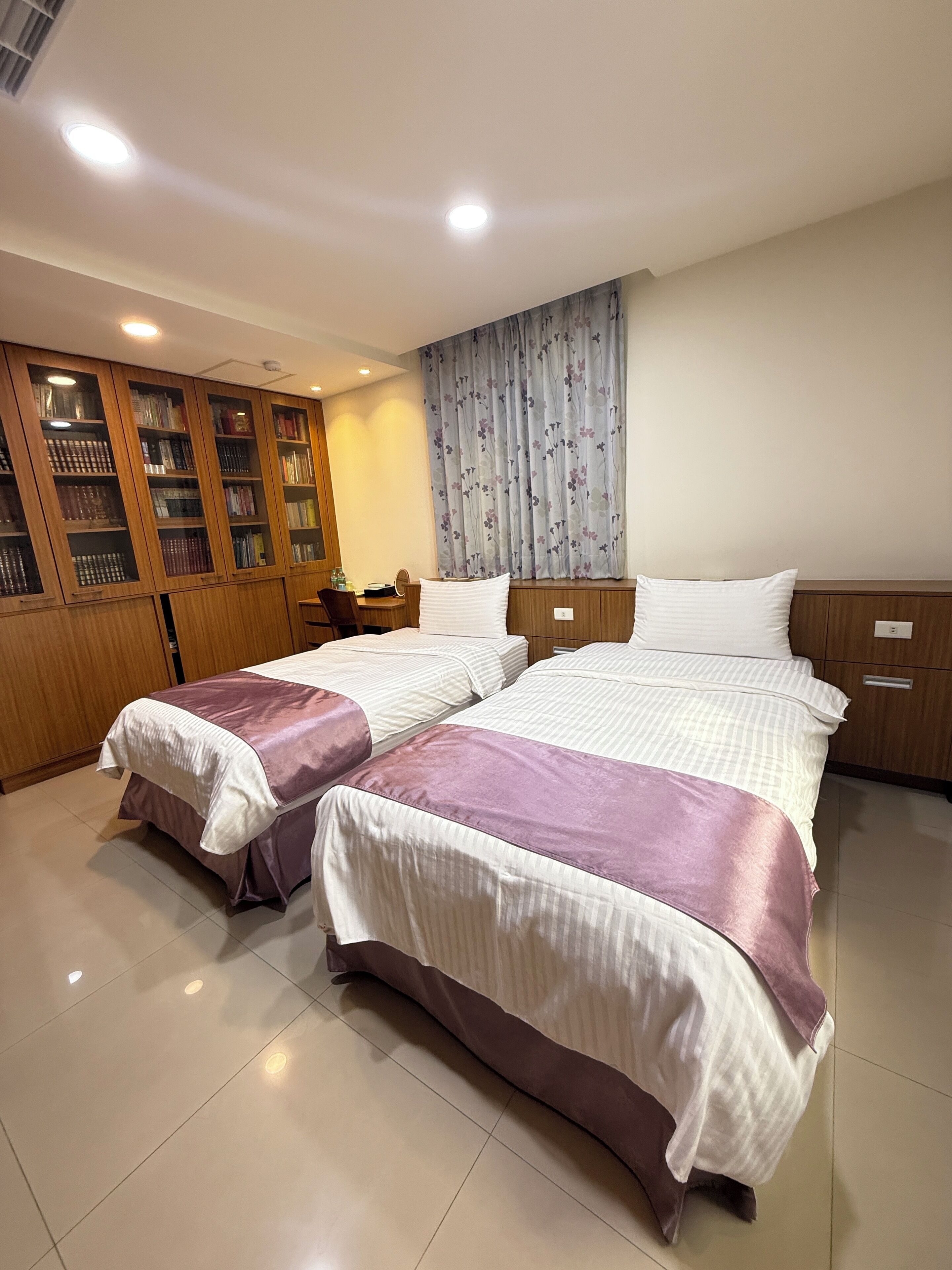 Quarto de hotel com duas camas, um guarda-roupa de madeira e uma escrivaninha com cadeira.