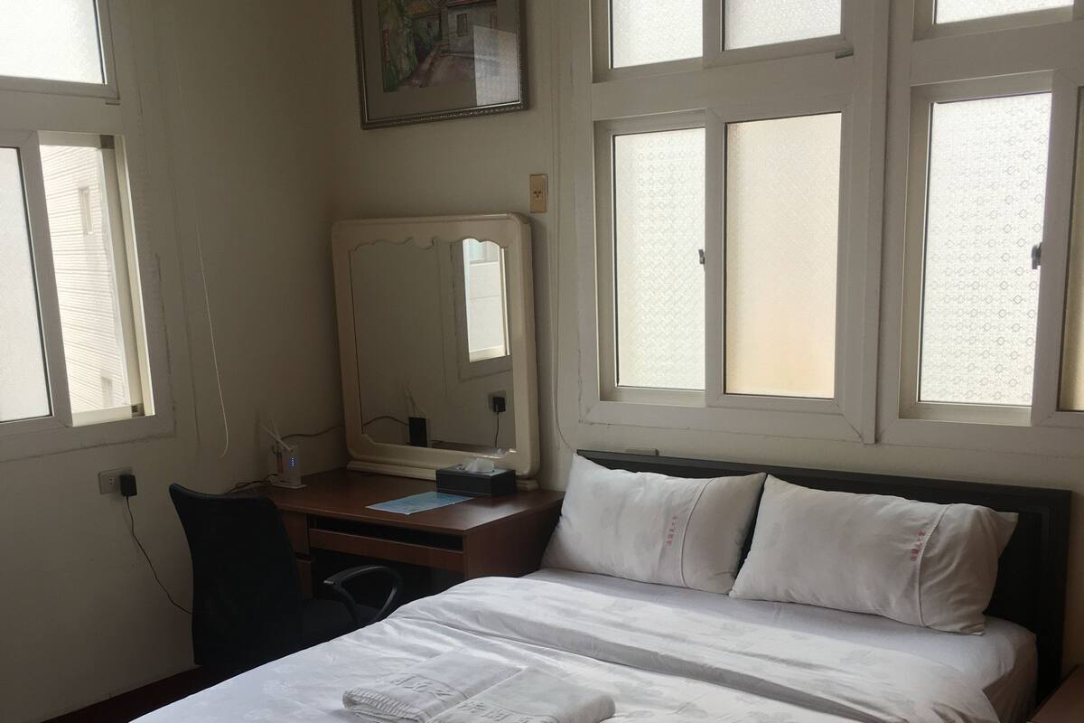 Ein Schlafzimmer mit Bett, Schreibtisch, Stuhl und einem Fenster mit Jalousien.