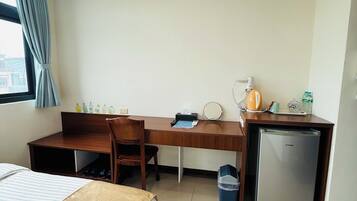 A hotel room with a bed, a desk, a chair, a small refrigerator, and a window with curtains.