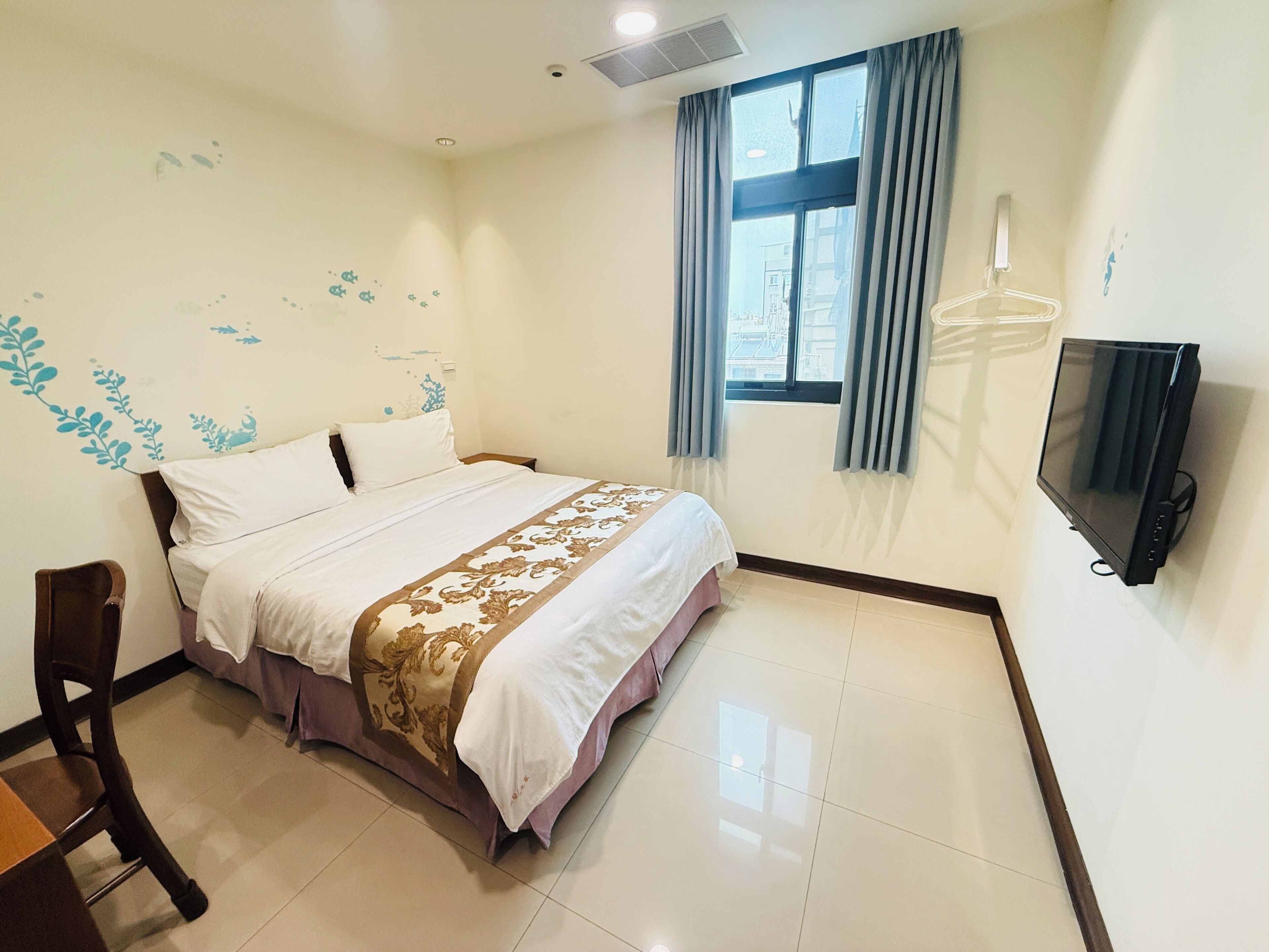 A hotel room with a bed, a chair, a TV, and a window with curtains.