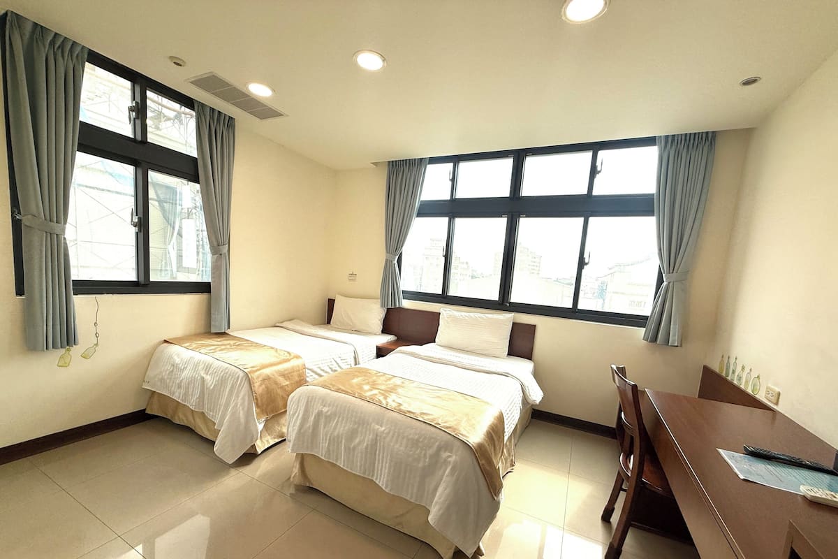 Ein Hotelzimmer mit zwei Betten, einem Schreibtisch und großen Fenstern.
