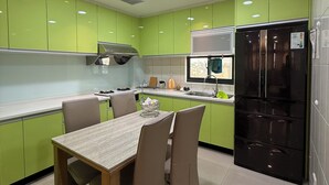 A modern kitchen with green cabinets, a black refrigerator, and a dining area with a table and chairs. - Frank's Hostel (Jincheng)