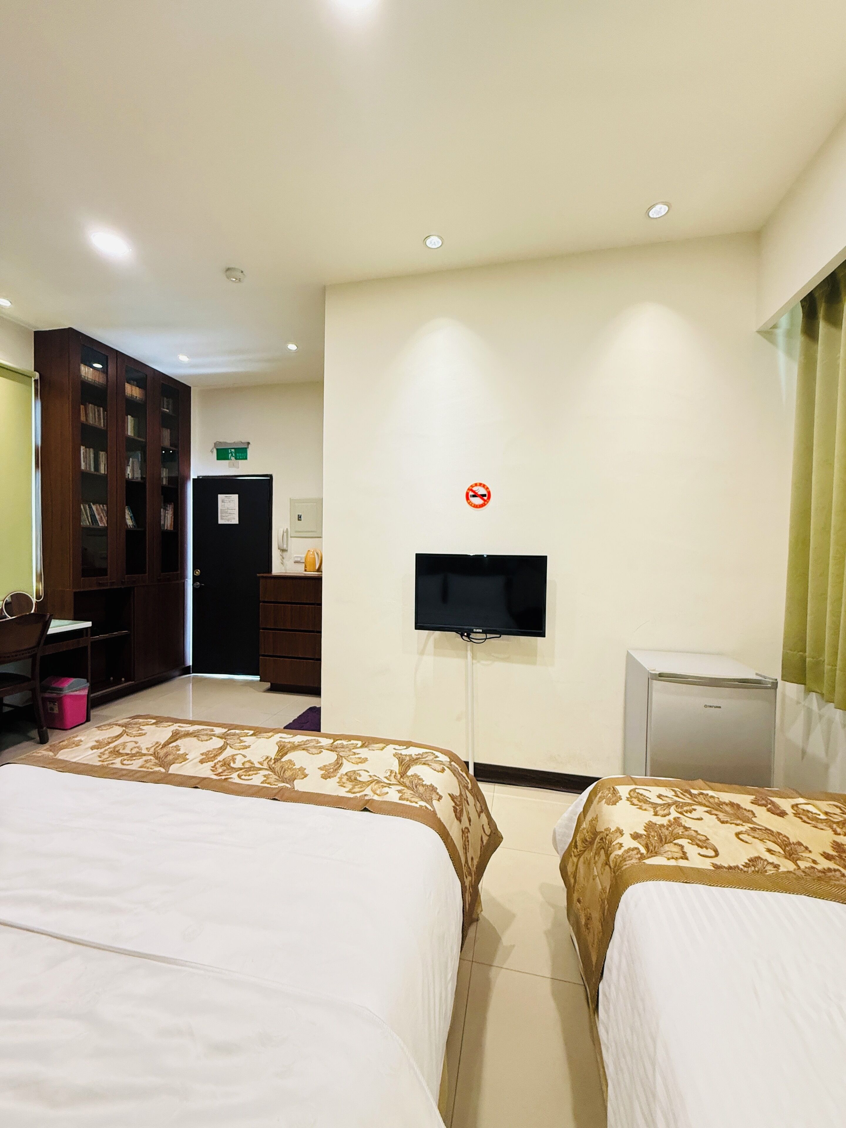 Habitación de hotel con dos camas, televisión, escritorio, armario y un refrigerador pequeño.
