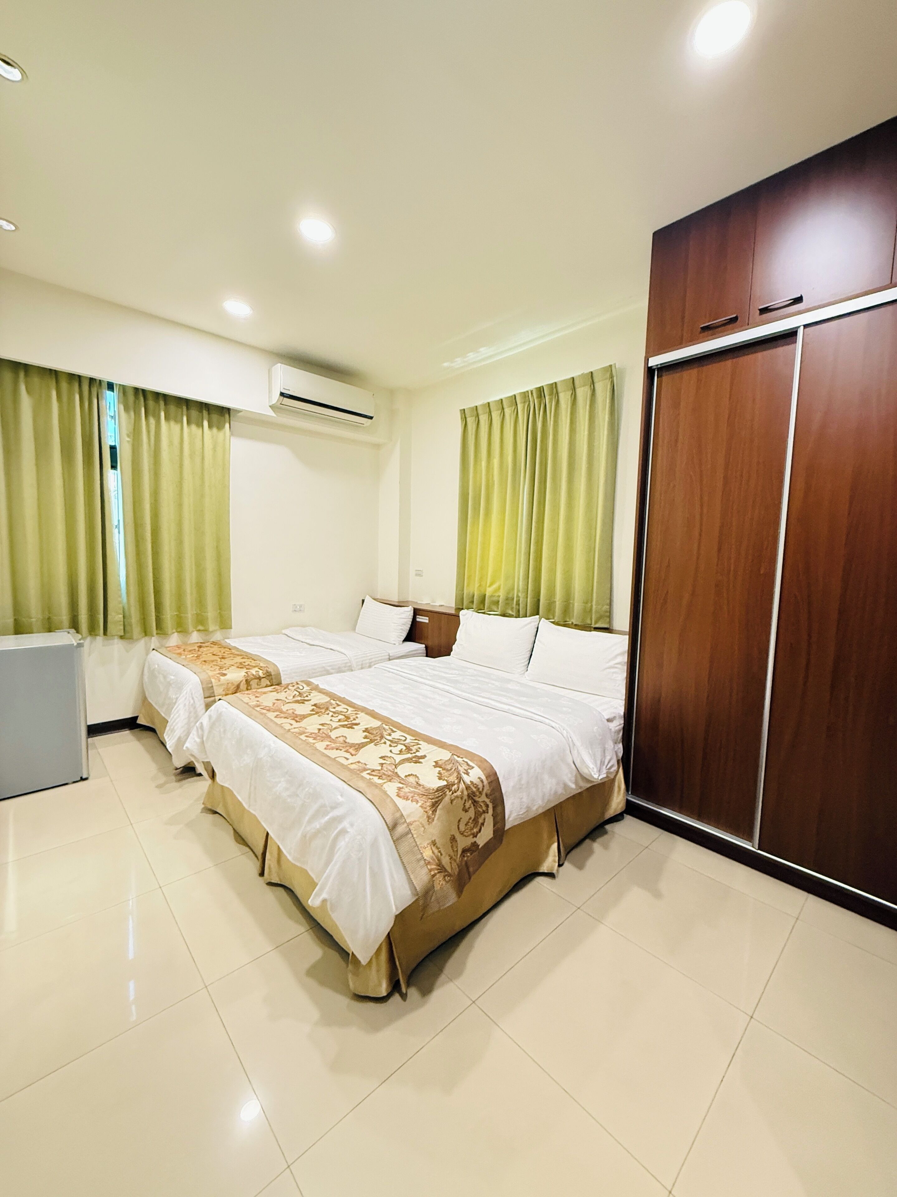 A hotel room with a large bed, a wardrobe, a desk, and an air conditioning unit.