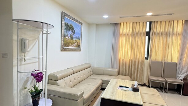 A modern living room with a beige sectional sofa, a round coffee table, and a glass shelving unit with a potted plant. - Frank's Hostel (Jincheng)
