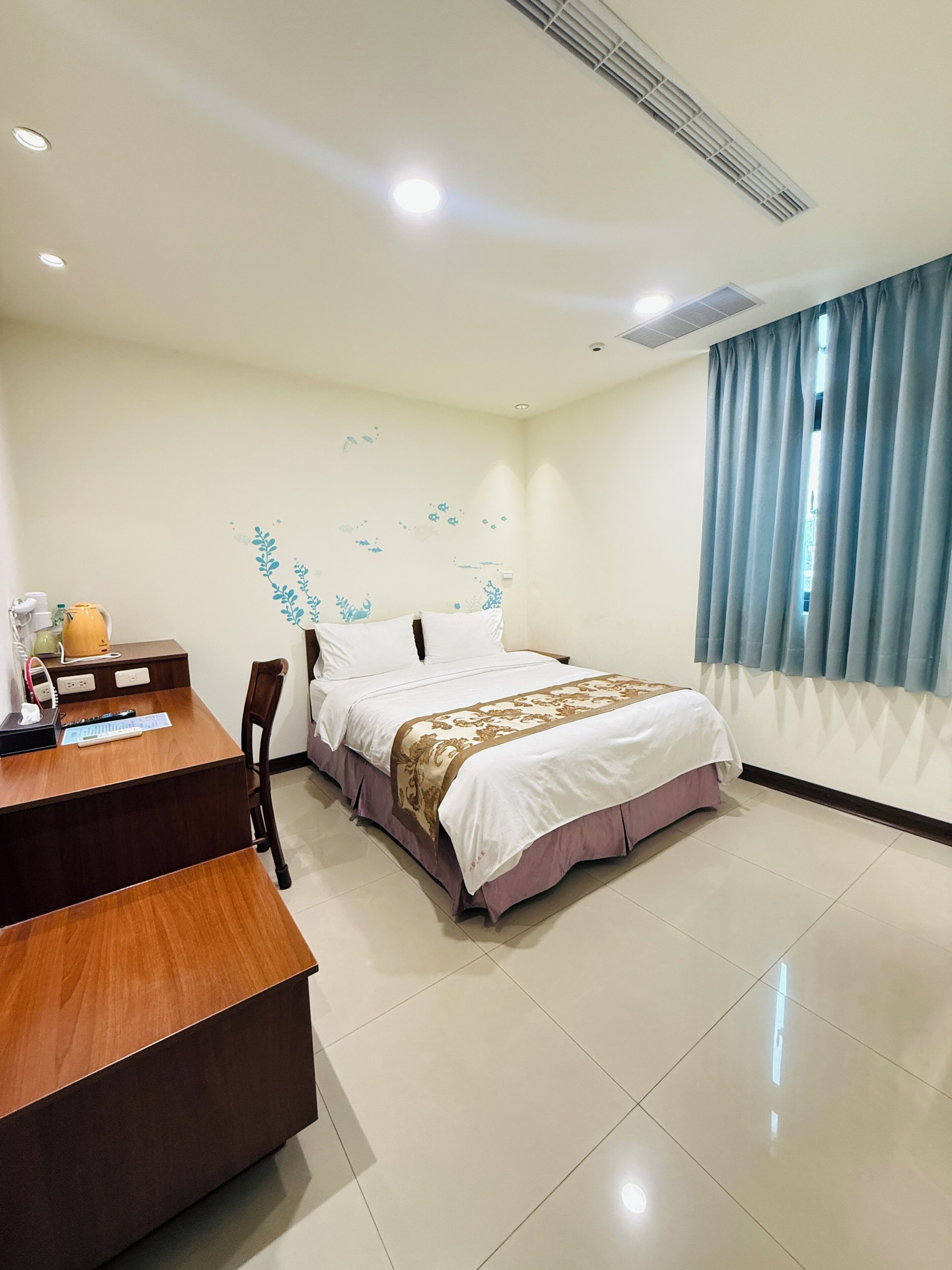 Habitación de hotel con cama, escritorio y silla. Se ve una ventana con cortinas.