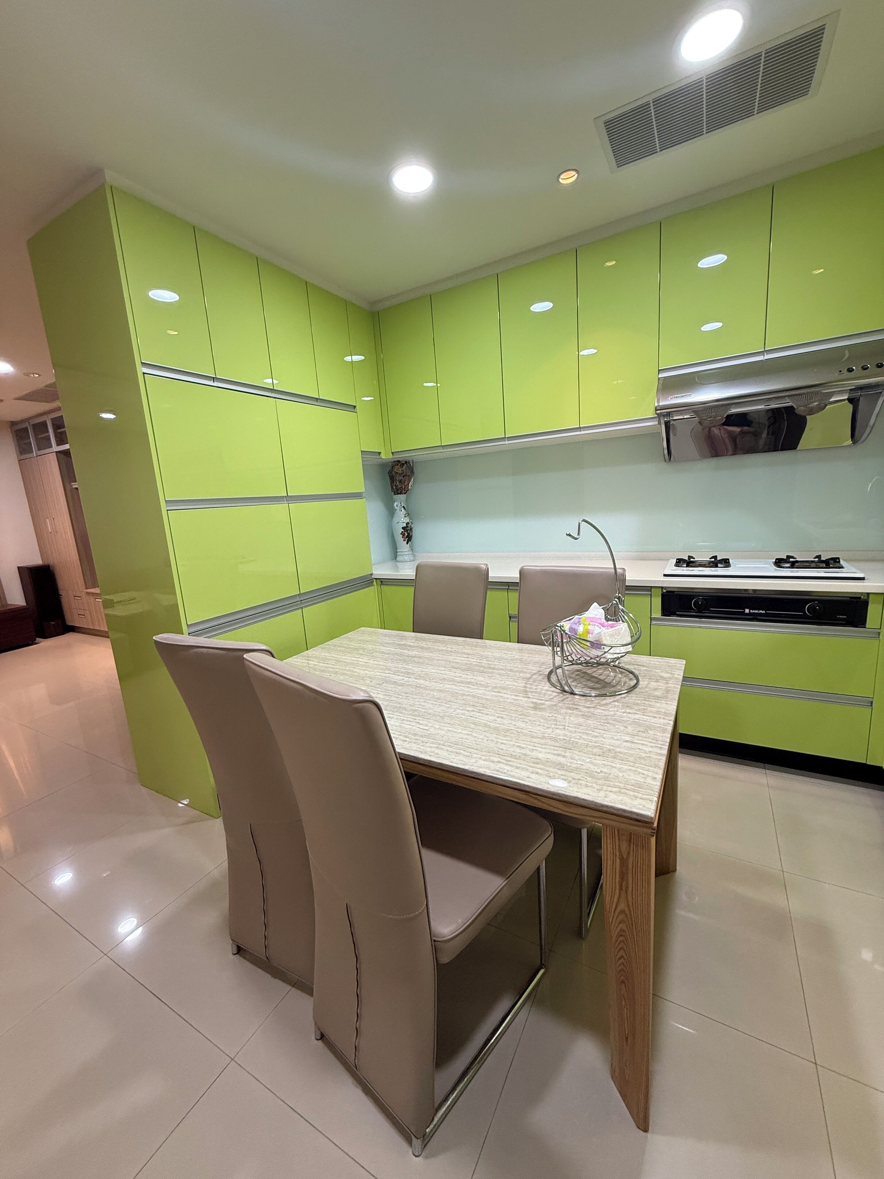 Una cocina moderna con armarios verdes, encimera de mármol y zona de comedor con mesa y sillas.