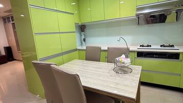 Una cocina moderna con armarios verdes, encimera de mármol y zona de comedor con mesa y sillas.