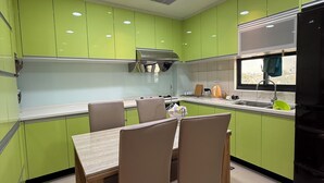A modern kitchen with green cabinets, a dining table with chairs, and a black refrigerator. - Frank's Hostel (Jincheng)