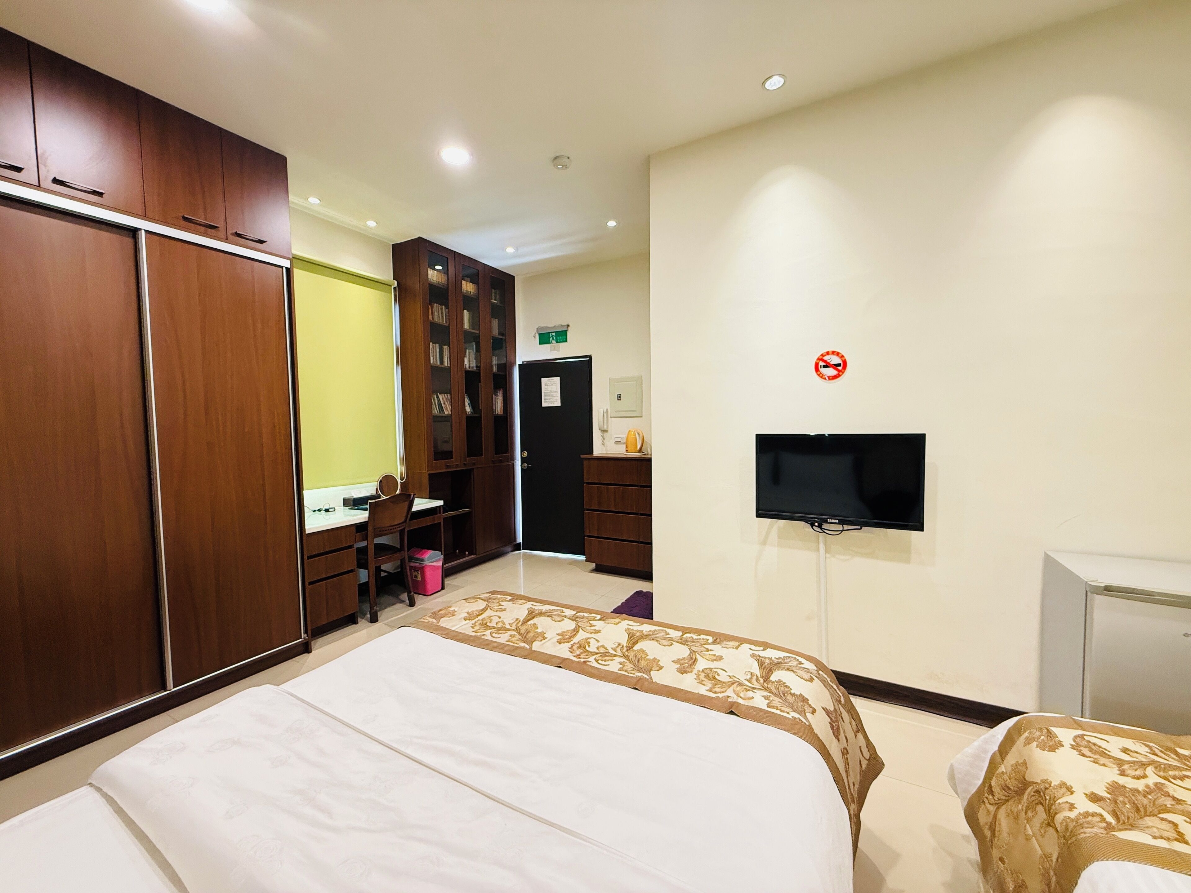 A hotel room with a bed, a desk with a chair, a wardrobe, a television, and a door with a sign.