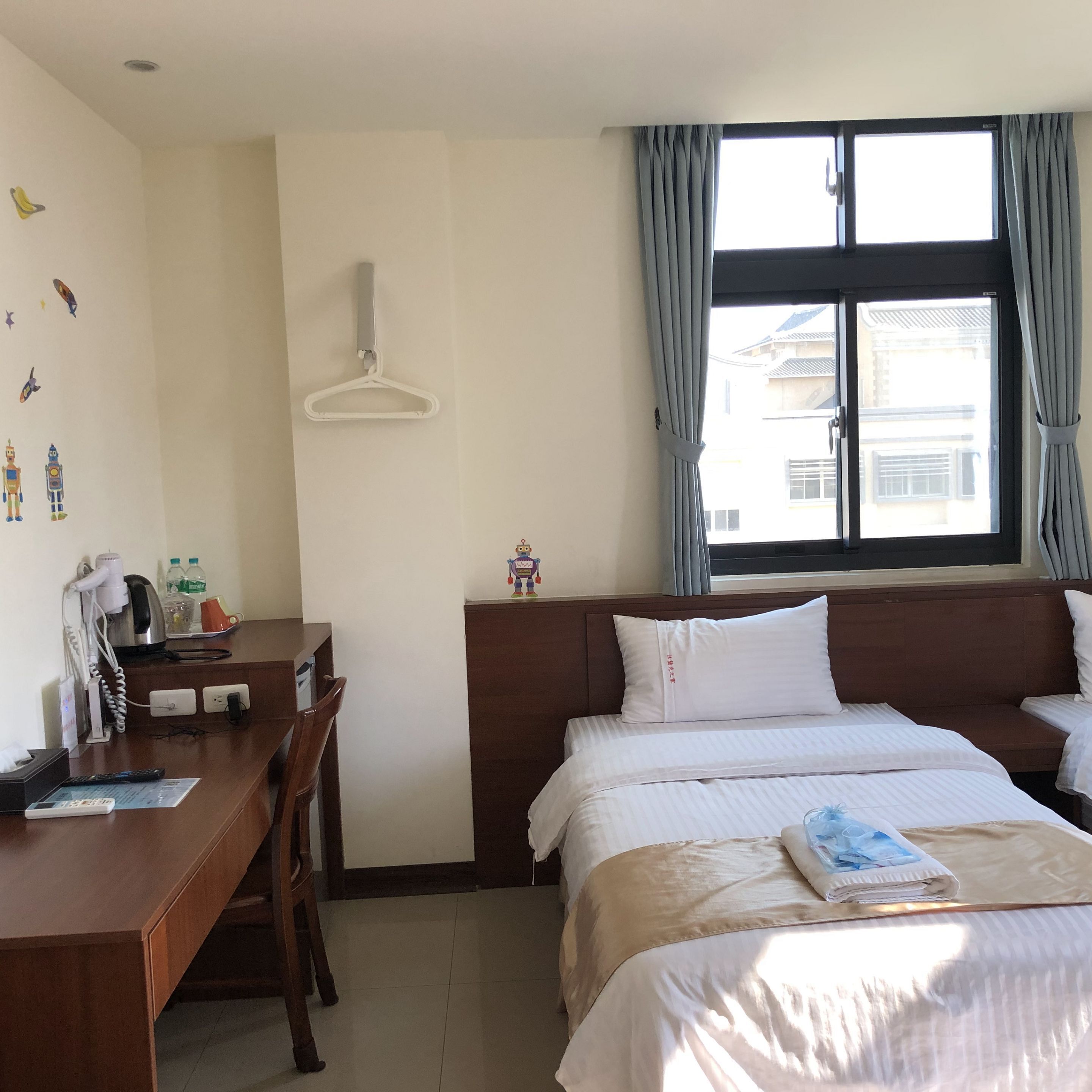 A hotel room with a bed, bedside table, desk, and a window with curtains.
