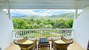 A balcony with wicker furniture and a table, overlooking a lush green landscape. - Baan Ing Khao (Pak Chong)