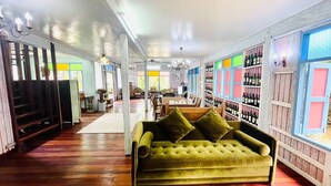 A spacious room with a wooden floor, a green sofa, and a wine rack with bottles. - Baan Ing Khao (Pak Chong)
