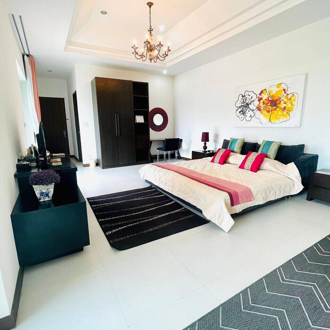 A modern bedroom with a large bed, a desk, a wardrobe, and a chandelier.