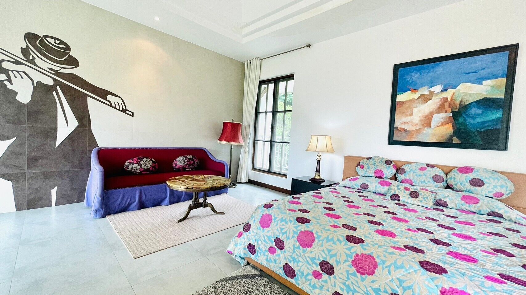 A bedroom with a bed, a sofa, a table, and a painting on the wall.