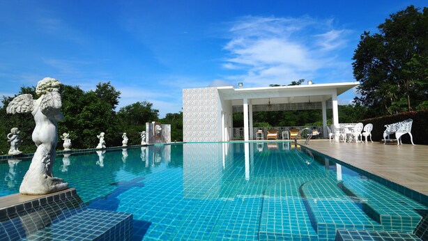 A swimming pool with tiled flooring, a statue, and a covered seating area with chairs. - Baan Ing Khao (Pak Chong)