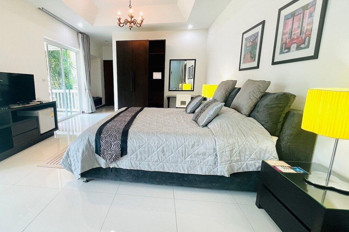 A modern bedroom with a large bed, a TV, a bedside table with a lamp, and a balcony with curtains.