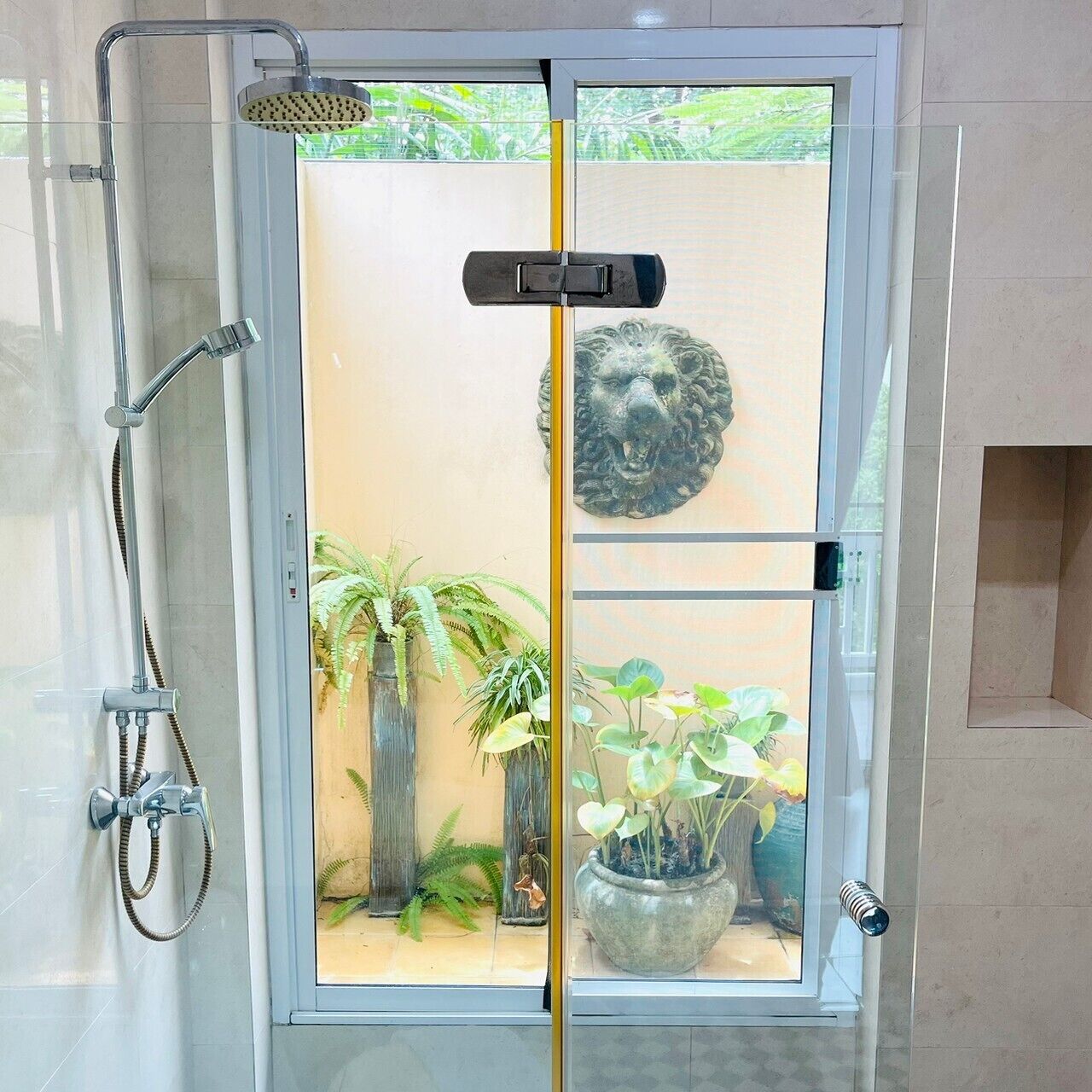 A glass-enclosed shower area with a visible plant and a decorative lion head on the wall.