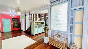 A room with wooden flooring, a white rug, a green cabinet with decorative items, and a window with blinds. - Baan Ing Khao (Pak Chong)