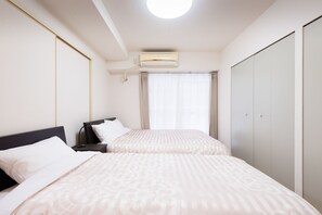 A hotel room with two beds, a wardrobe, an air conditioning unit, and a nightstand with a lamp. - Osaka Maison Rech (Osaka)
