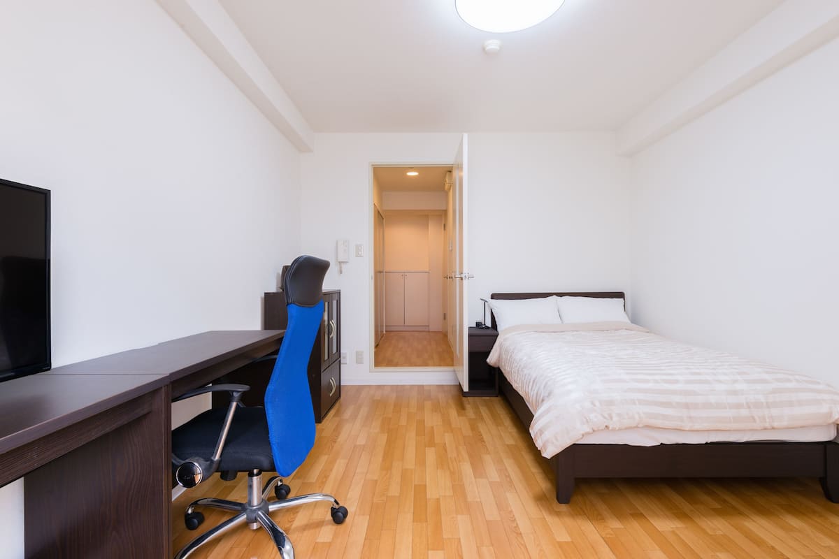 Un dormitorio con cama, escritorio con silla, televisor y armario.