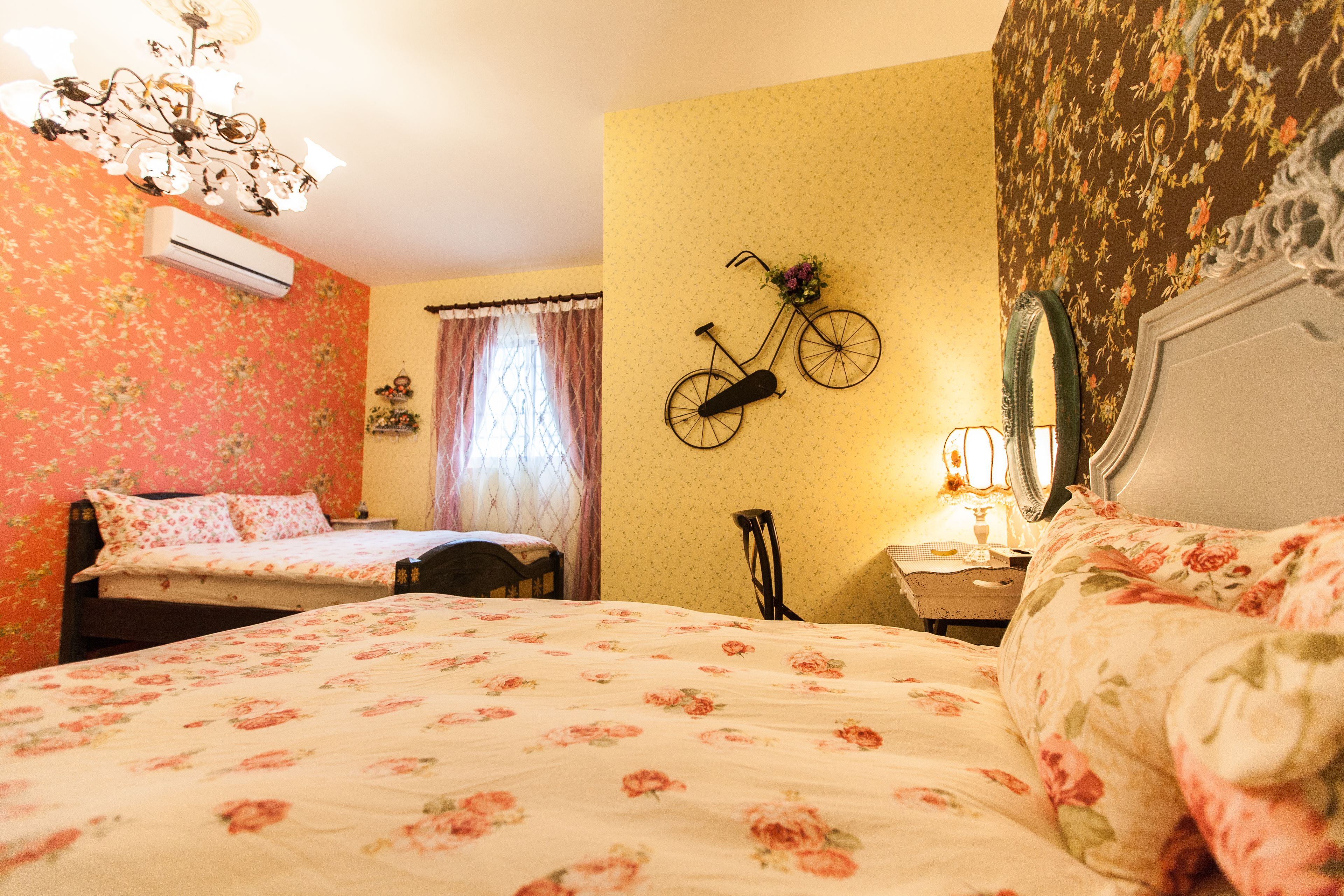 A bedroom with floral wallpaper, a bicycle wall decoration, a mirror, and a chandelier.