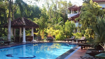 Ein Swimmingpool mit Liegestühlen und einem Pavillon, umgeben von üppiger Vegetation.