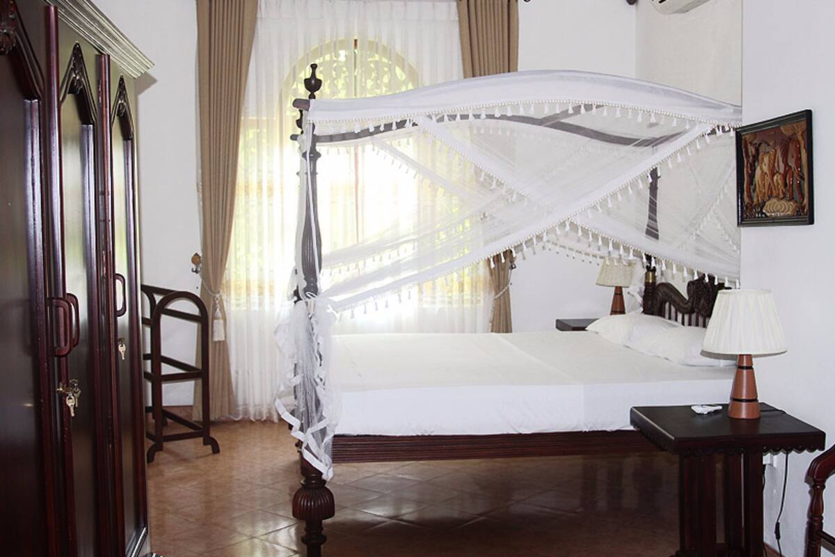 Una cama con dosel, una mesita de noche con lámpara, y un cuadro enmarcado en la pared.