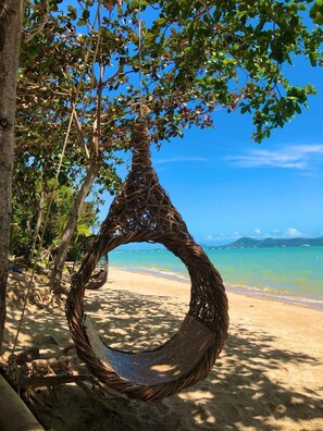 A beach scene with a hanging hammock made of natural materials, surrounded by trees and a clear view of the ocean. - Sea Safari (Rawai)