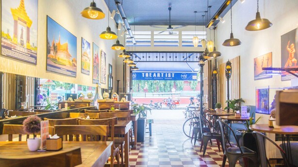 Interior de restaurante con mesas y sillas de madera, lámparas colgantes y cuadros en las paredes.