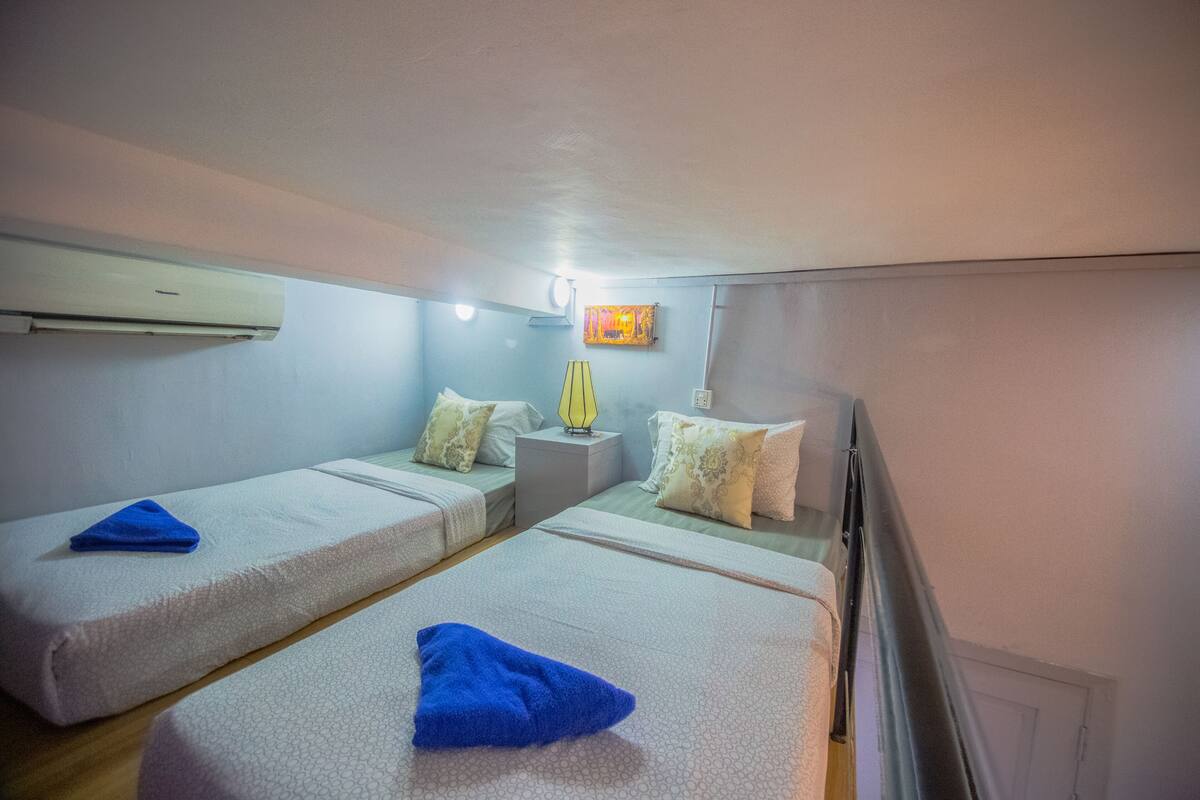 Ein kleines, kompaktes Zimmer mit zwei Einzelbetten, einem Nachttisch mit Lampe und einer Wand-Klimaanlage.