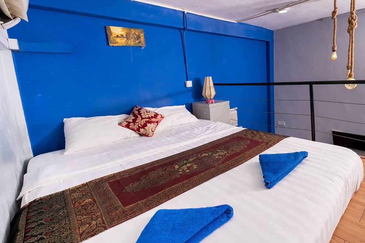 Ein modernes Hotelzimmer mit einem großen Bett, blauen Wänden, einem rot-goldenen Teppichläufer und einem gerahmten Bild an der Wand.