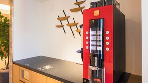 Eine Kaffeemaschine mit rotschwarzem Design, eine Wanddekoration aus Holz und eine schwarze Arbeitsplatte.