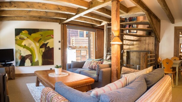 A cozy living room with a sofa, a coffee table, and a television. There is a painting on the wall and a wooden staircase.