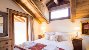A bedroom with a large bed, two bedside tables with lamps, a wooden ceiling, and a window with curtains.
