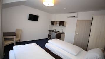 Une chambre d’hôtel avec deux lits, un bureau, une chaise, une télévision, un coin cuisine et une armoire.