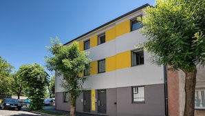 En flervåningsbyggnad med modern design, som kännetecknas av en kombination av vita och gula fasader, samt en parkeringsplats med bilar och träd.