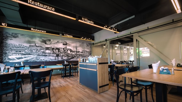 En modern restaurang med träbord och stolar, en väggmålning och en bardisk.