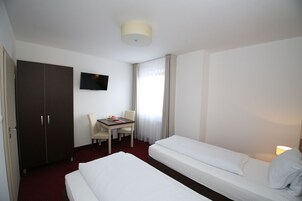 Habitación de hotel con dos camas, un escritorio con silla, un televisor y un armario.