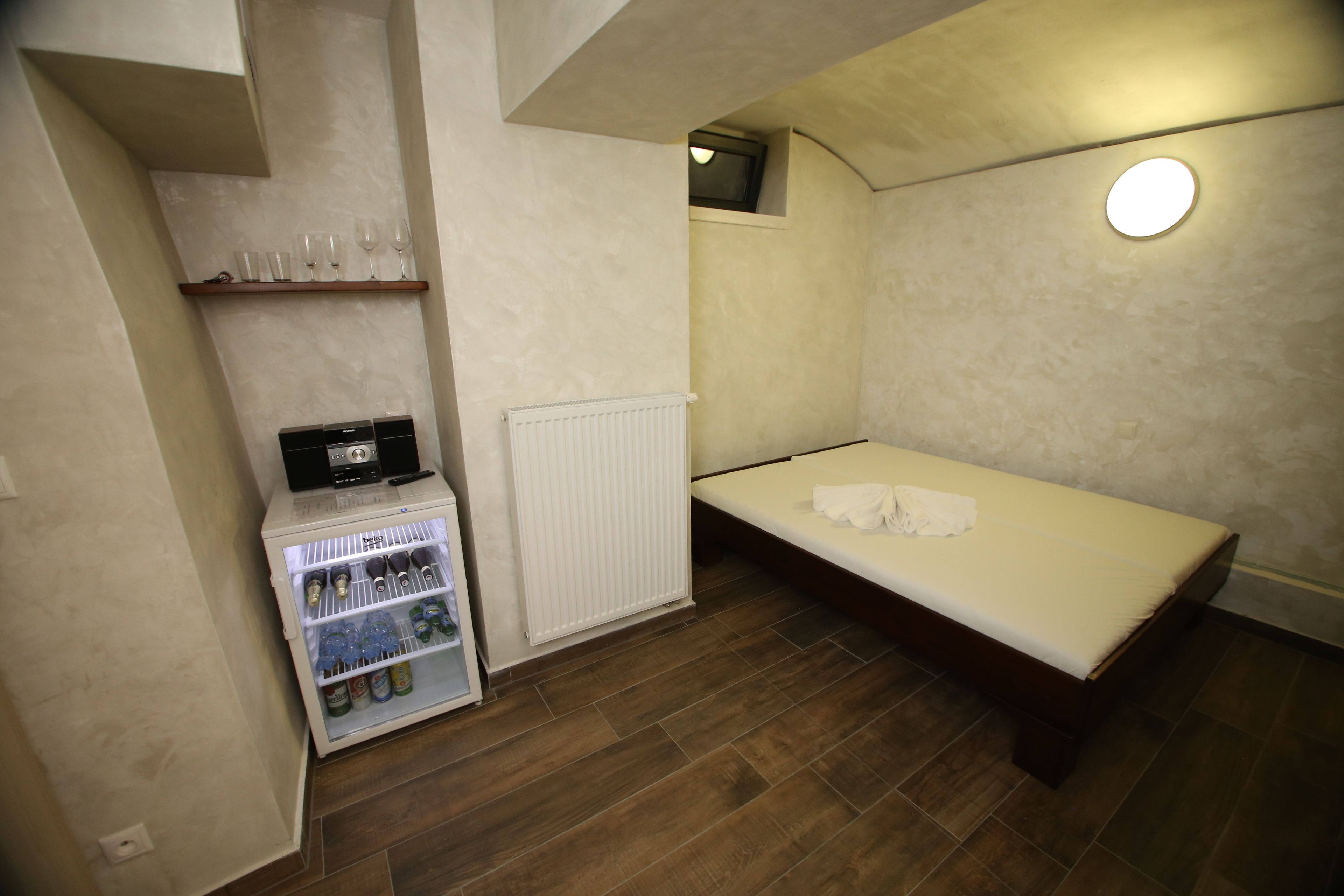 Een kleine, compacte kamer met een bed, een plankje met glazen en een minibar met drankjes.