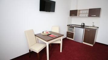 Cocina compacta con una mesa y sillas, un televisor de pantalla plana y piso cubierto de alfombra roja.