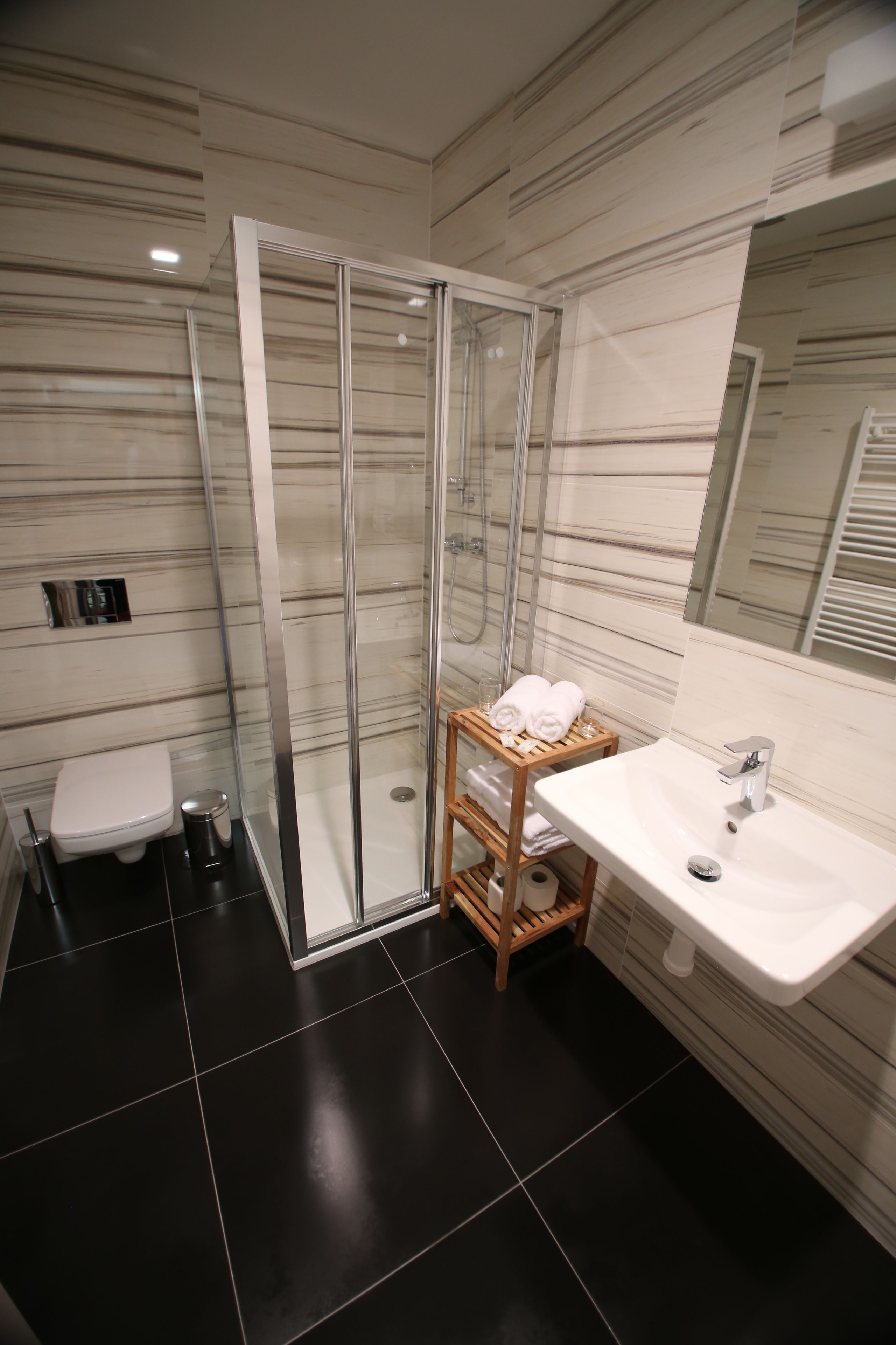 Une salle de bain moderne avec une douche à parois de verre, un lavabo blanc et une étagère en bois où sont posées des serviettes.