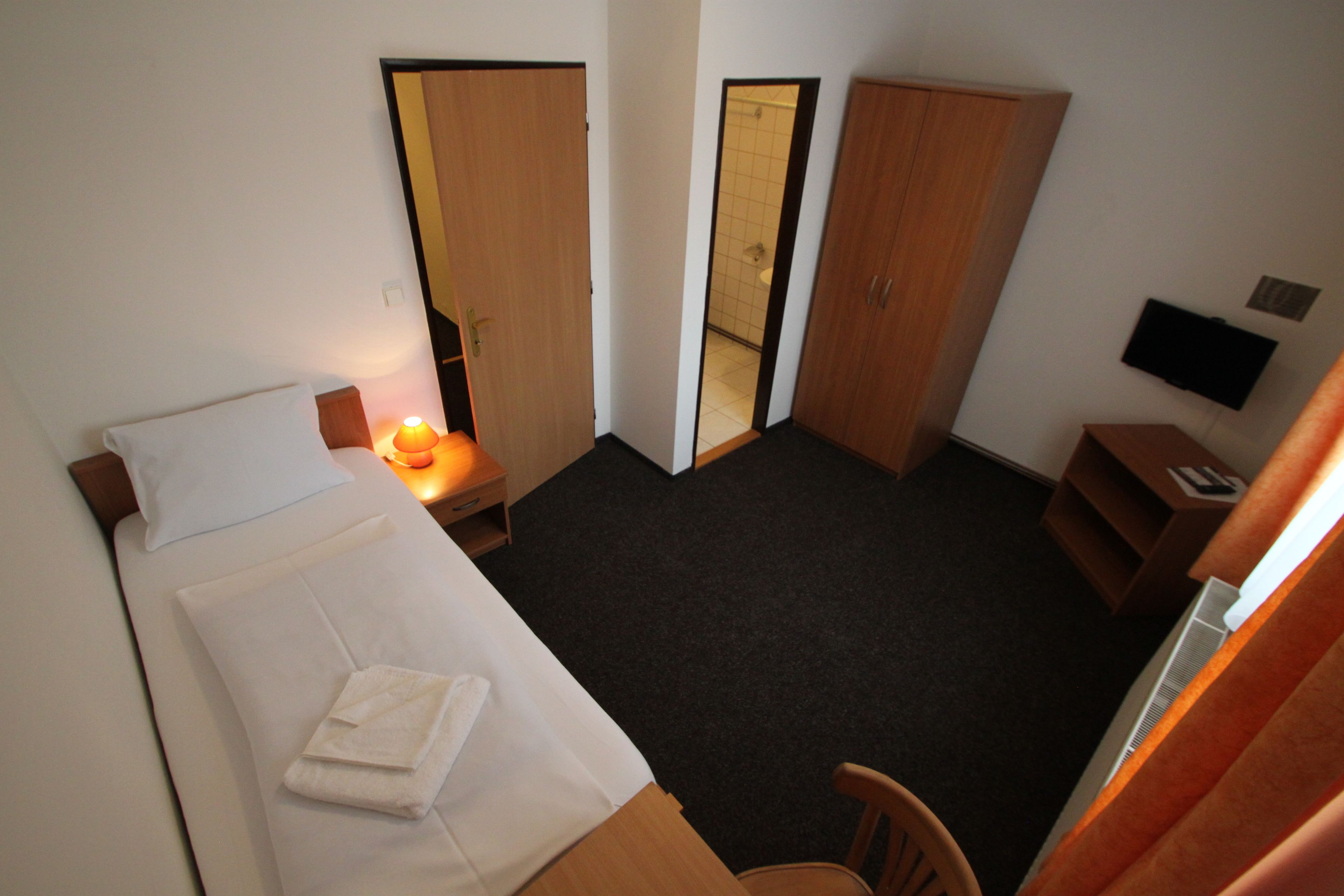 Una habitación de hotel con una cama individual, un escritorio, una silla y un armario.