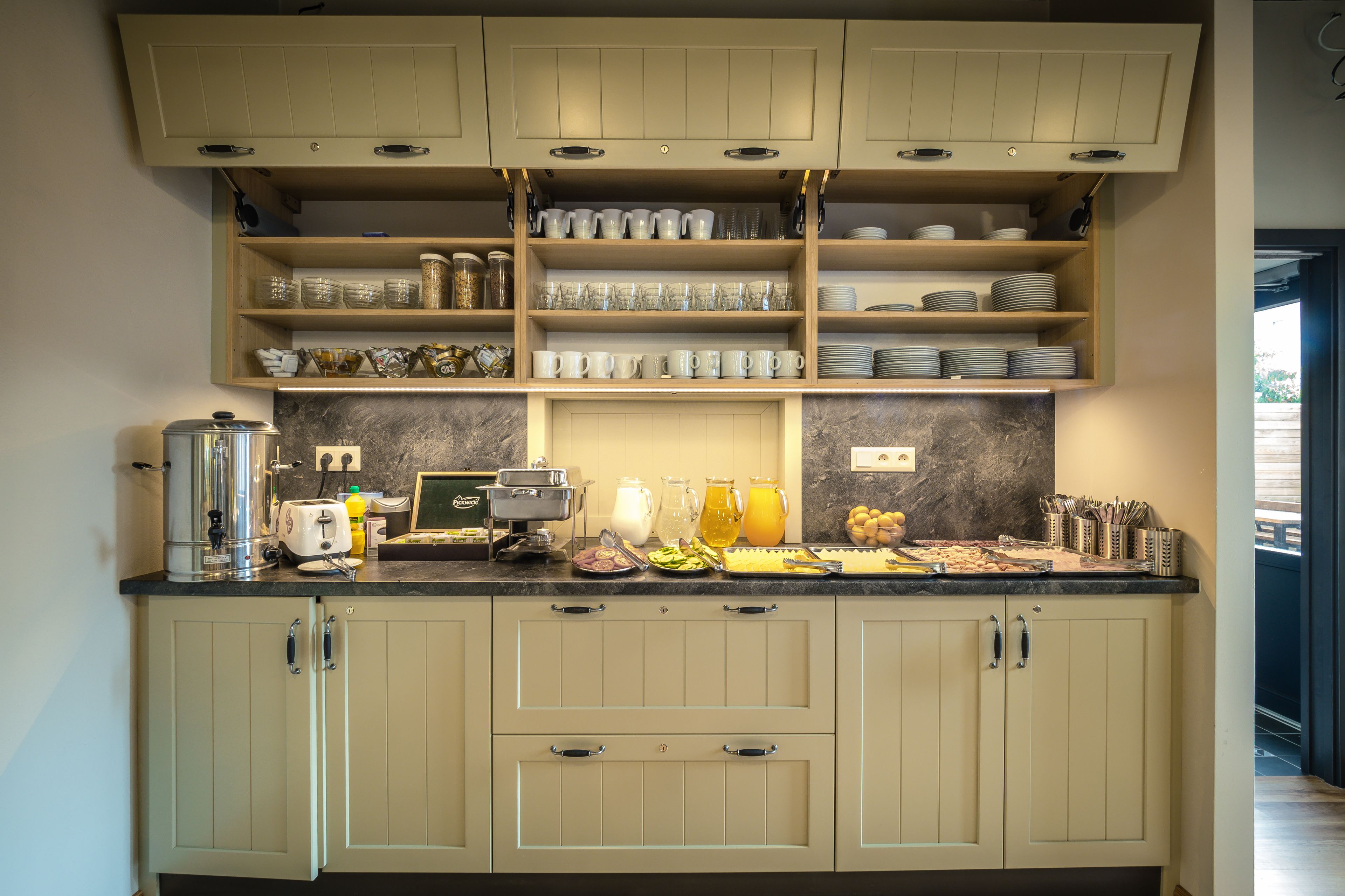A kitchen with light-colored cabinets, a marble backsplash, and various kitchen appliances and utensils on the countertop.
