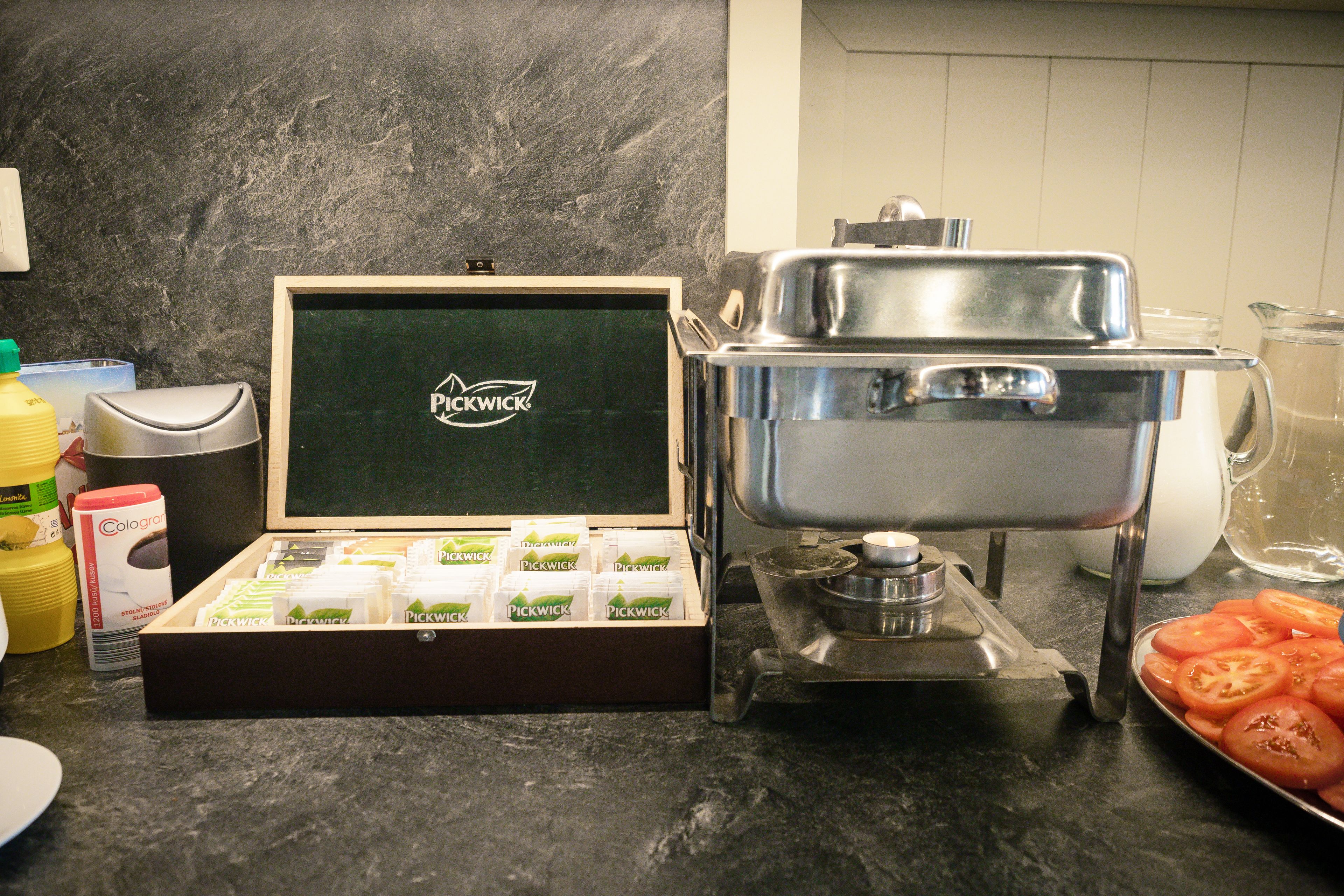 A kitchen counter with a box of Pickwick tea, a stainless steel pot, and a tray of sliced tomatoes.