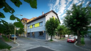 A two-story residential building with a yellow and grey facade, a visible garage door, and a tree-lined street. - Penzion U Gigantu (Plzen)