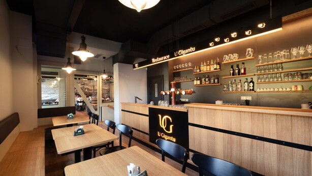 A restaurant interior with wooden tables and chairs, a bar area with shelves of bottles and glasses, and a large illuminated sign reading "U Gigantu". - Penzion U Gigantu (Plzen)