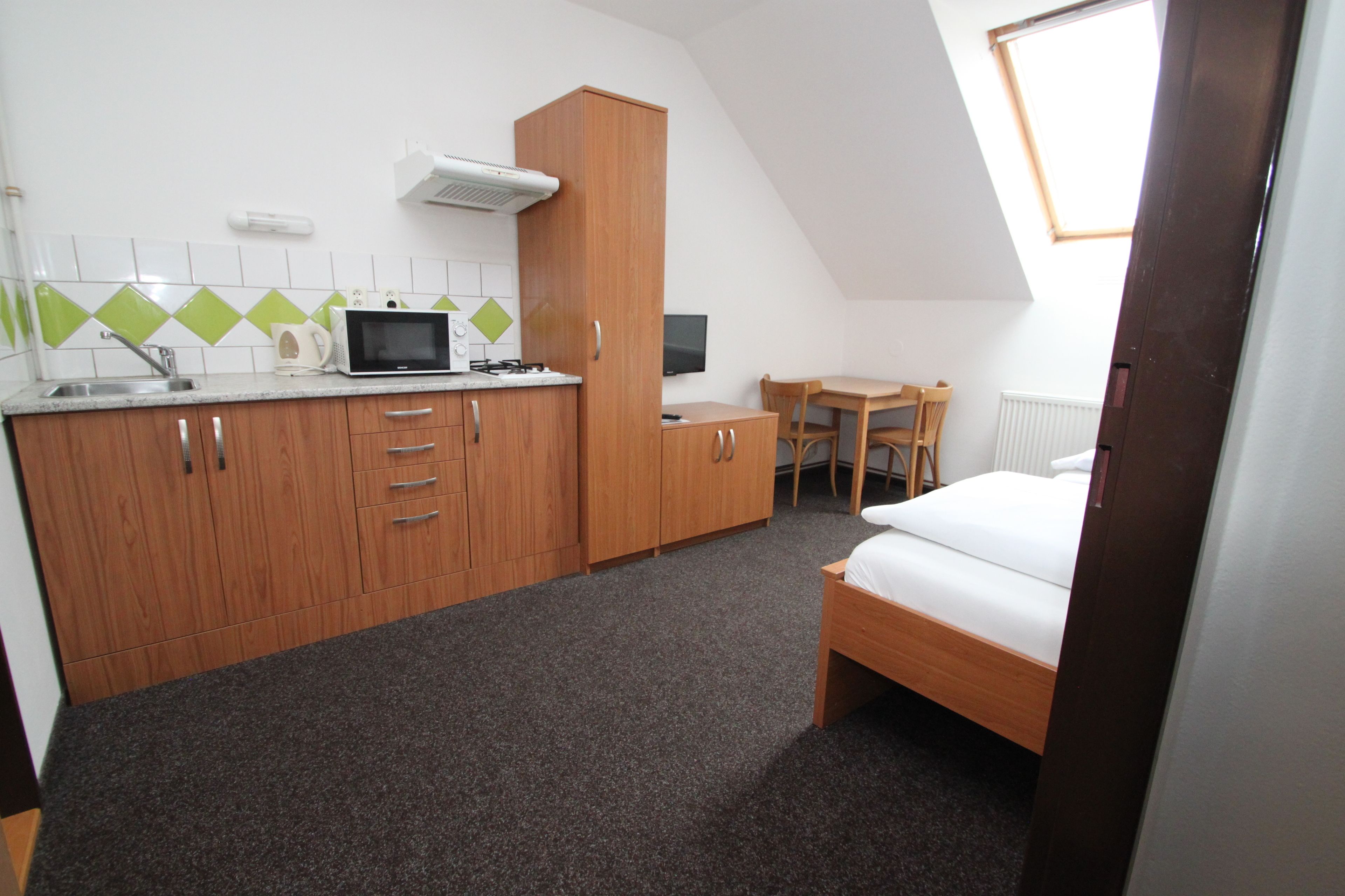 Una habitación pequeña con kitchenette, una cama, una mesita y una silla.