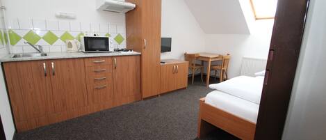 Una habitación pequeña con kitchenette, una cama, una mesita y una silla.